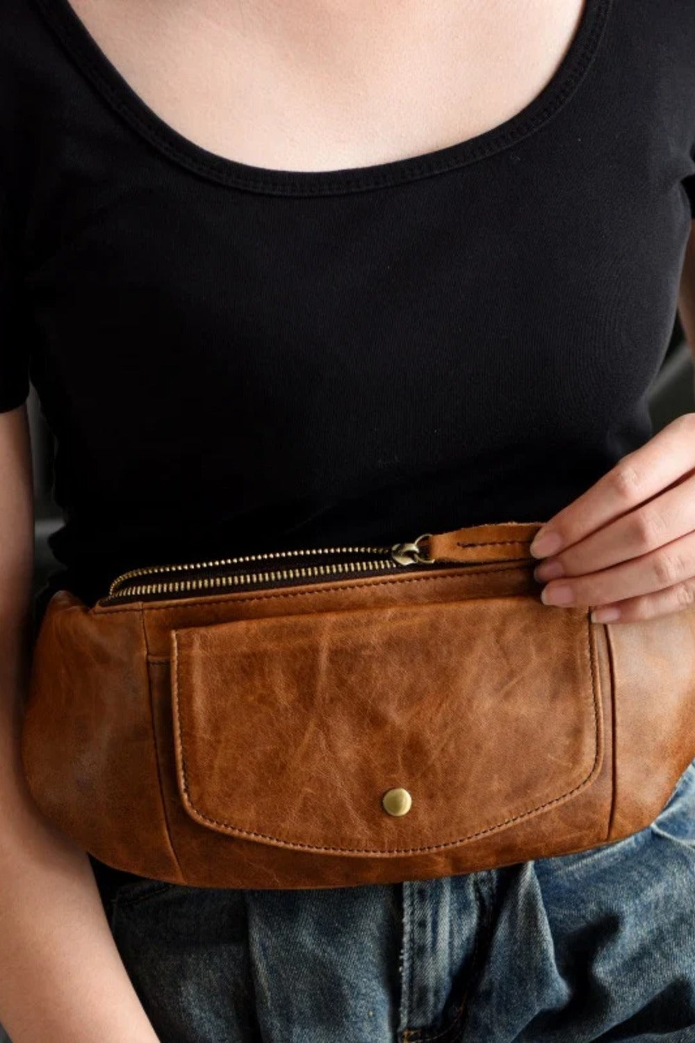Close view of the tan leather sling bag worn as a belt bag at the waist over jeans