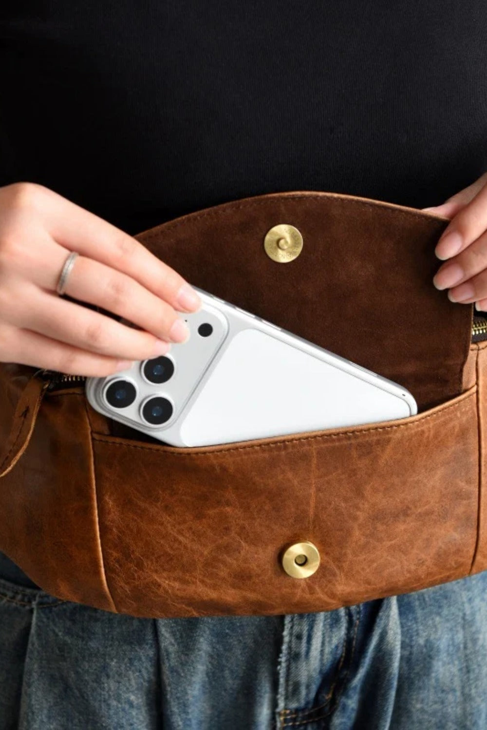 The tan leather sling bag open with a smartphone inside, showing everyday carry capacity