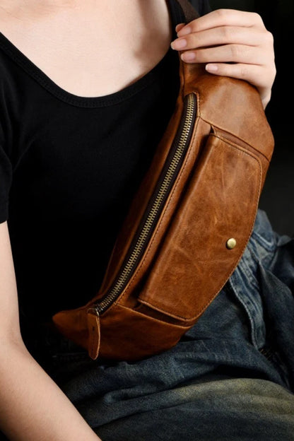 Tan leather sling bag worn crossbody over the chest, hand resting on the strap